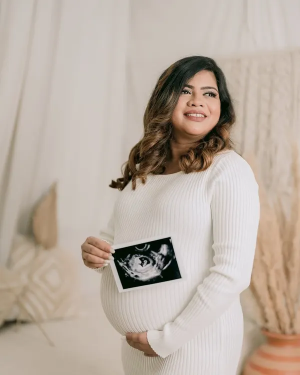 A portrait of a glowing mother-to-be. Holding her sonogram picture, she looks towards the future with a happy and hopeful expression, beautifully captured in a bright, airy studio.