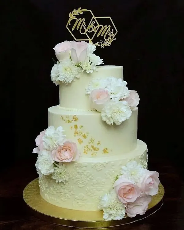There is something timeless about a three-tier wedding cake. This one features delicate stenciled buttercream, fresh pink and white roses, and a custom "Mr & Mrs" topper, making it a classic and romantic choice for a wedding.