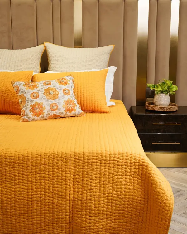 A beautifully made bed with vibrant yellow and orange bedding against a modern, textured headboard. This shot creates a warm and inviting atmosphere, perfect for showcasing a bold home collection.