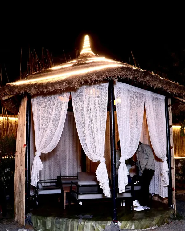 Your own private corner under the stars. This is one of our bamboo cabanas at night, perfect for intimate conversations or a quiet dinner. The sheer curtains and warm lighting create a cozy, secluded feel.