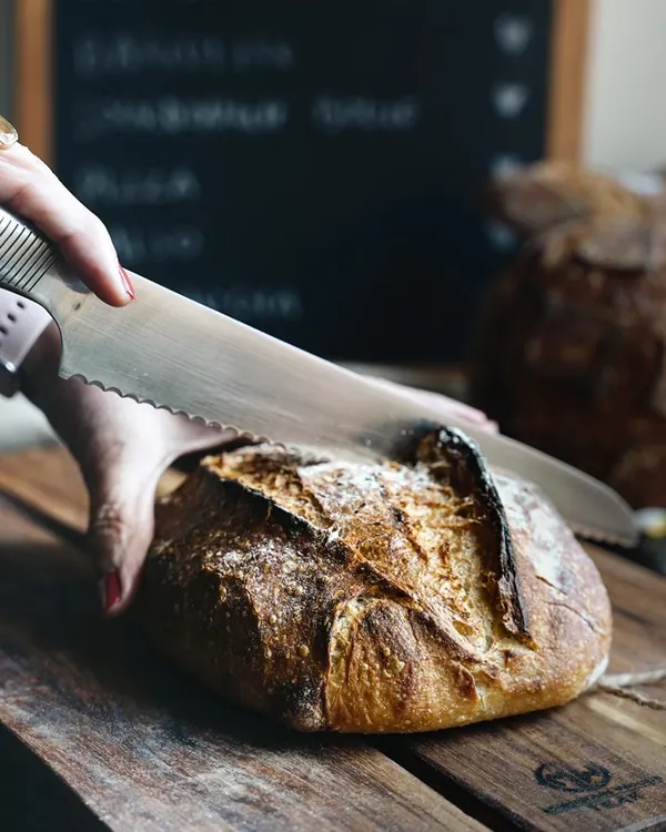 Slicing into this beauty is like unwrapping a gift. This action shot captures the satisfying moment of cutting into a freshly baked sourdough loaf, revealing the crusty exterior and soft crumb.