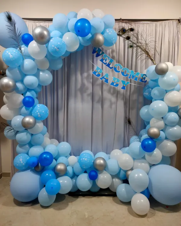A beautiful circular balloon arch in shades of blue, white, and silver, with a 'Welcome Baby' banner. This setup is perfect for creating a photo corner at home.