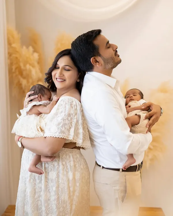 Welcoming newborn twins is double the blessing. In this serene studio portrait, a new mother and father stand back to back, each cradling one of their tiny miracles, capturing a moment of quiet joy and connection.