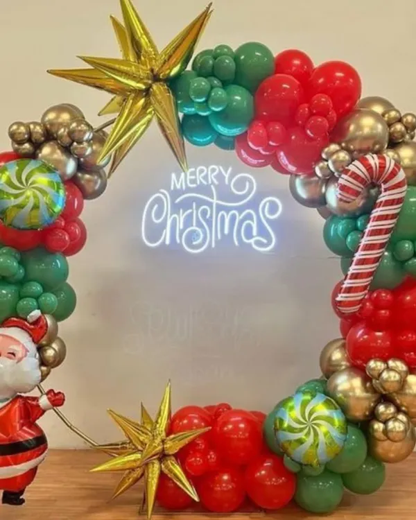 A festive Christmas wreath made entirely of balloons. This one features red, green, and gold balloons, a 'Merry Christmas' neon sign, star-shaped foils, and a cute Santa Claus figure.