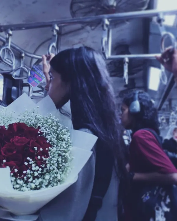 A quiet moment amidst the chaos of a Mumbai local train. A young woman holds a bouquet of red roses, lost in thought, showing how personal stories unfold even in the most public spaces.