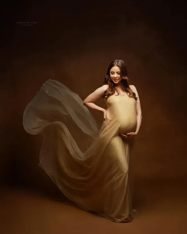 A classic maternity pose in a flowing golden gown. We use fabric tossing to create a sense of movement and drama, making you look and feel like a goddess.