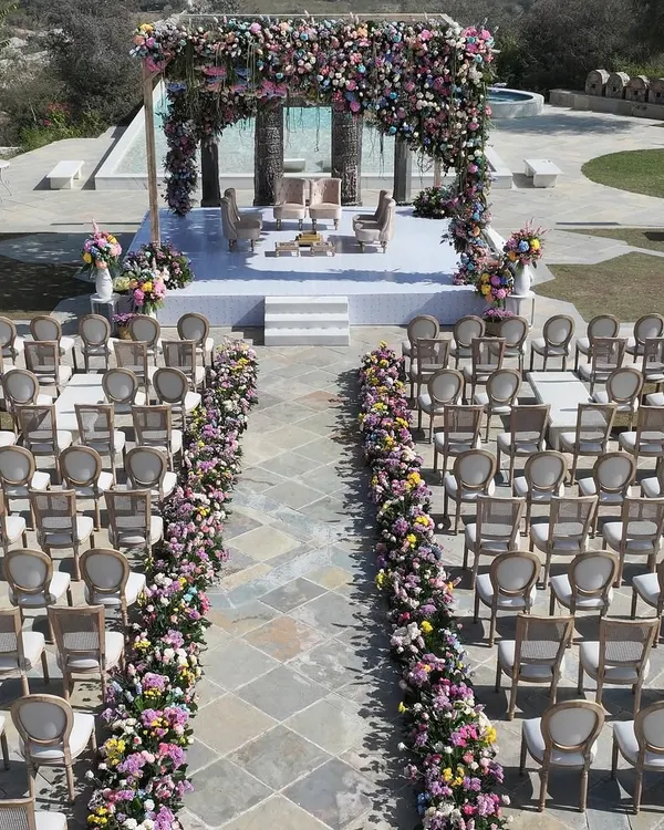 An aerial view showcasing the perfect symmetry of this pastel floral wedding ceremony. The aisle, lined with lush ground-level arrangements, leads the eye directly to the magnificent mandap, creating a breathtaking journey for the bride's entrance.