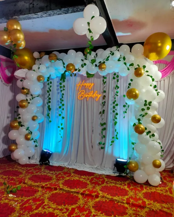 This jungle or nature-themed birthday backdrop is perfect for a first birthday. We use a white balloon arch decorated with green vines, a 'Happy Birthday' neon sign, and blue uplighting to create an enchanting forest look.