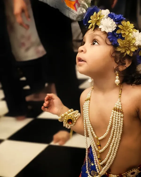 A candid shot of a young child in a Krishna costume, looking up with wonder. This is the essence of genuine childhood photography, capturing their natural curiosity during a festival celebration.