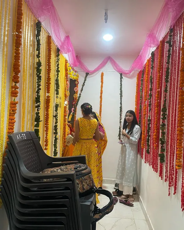 A beautiful entrance decoration for a Griha Pravesh using strings of fresh yellow and red marigold flowers and pink chunni fabric. This creates a traditional and welcoming feel.