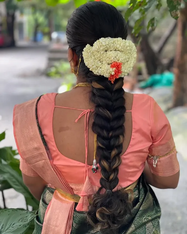 A classic South Indian bridal braid, neatly woven and adorned with a semi-circle of fresh jasmine and a touch of orange kanakambaram flowers. This hairstyle is timeless and elegant.