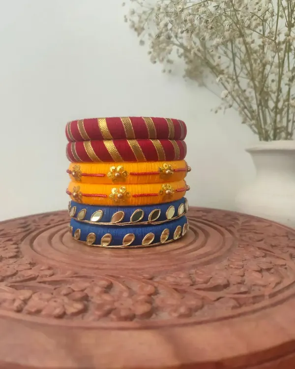 A vibrant stack of my handmade thread bangles. This set includes red and gold stripes, yellow with floral motifs, and blue with mirror work.