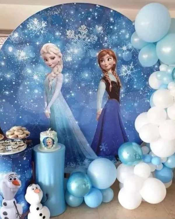 A magical Frozen themed birthday party featuring Elsa and Anna on a sparkling winter backdrop. The decor is completed with a blue and white balloon garland and themed pedestals for the cake and treats.