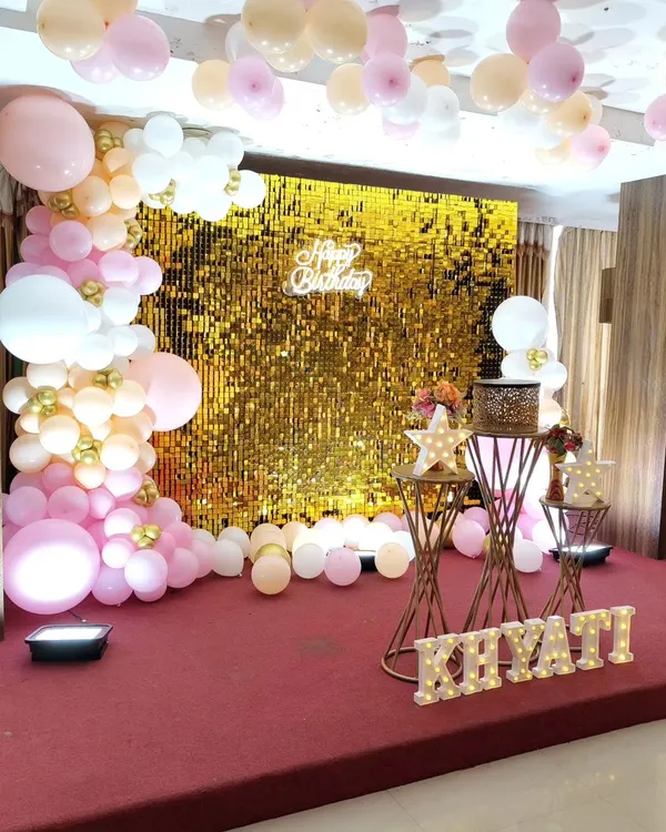A stunning gold sequin wall creates a glamorous backdrop for this birthday party, perfectly complemented by a pink and white balloon garland and marquee letters.
