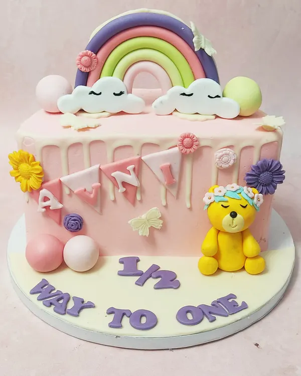 We celebrate the halfway mark to a big milestone with this adorable "halfway to one" cake. A sleepy teddy bear, a pastel rainbow, and a sweet banner adorn this pink drip cake, making it a perfect way to mark six months.