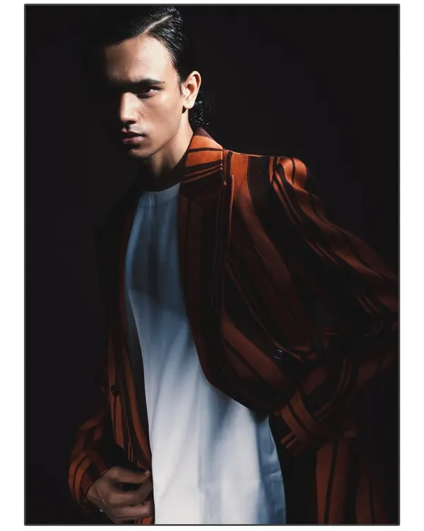 A tight, intimate portrait from the 'Silhouette' series, where dramatic light falls across half of the model's face. The deep shadows create a powerful, moody atmosphere that emphasizes his features and the texture of the jacket.