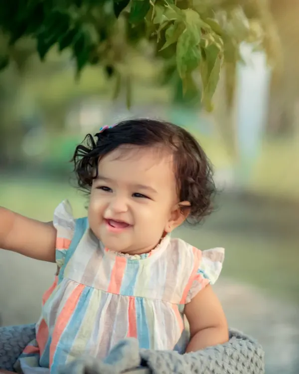 A beautiful outdoor portrait capturing a moment of pure, uninhibited laughter. The natural light and green background make this little girl's happy expression shine even brighter.