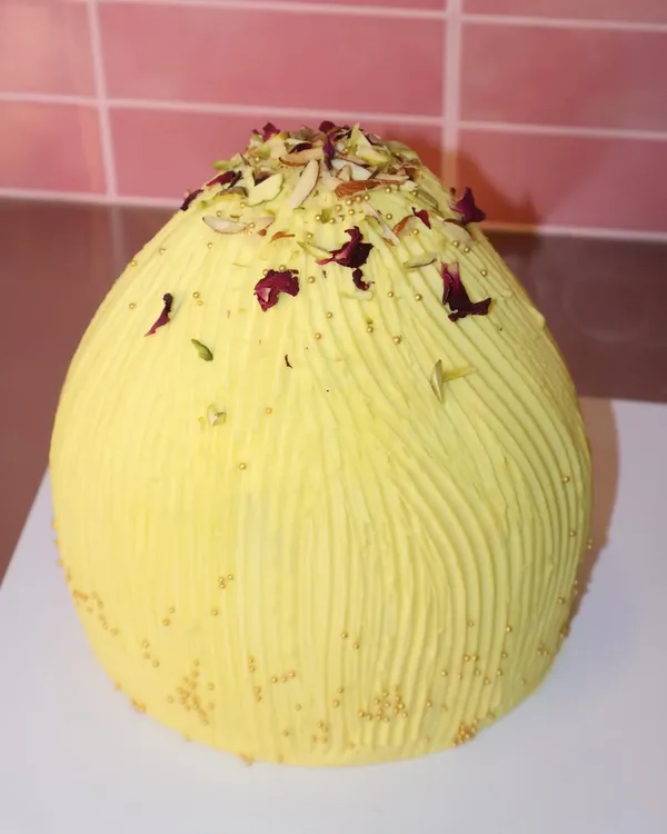 Celebrating Ganesh Chaturthi with our creative modak-shaped cake. This one is covered in yellow frosting with a textured finish and topped with pistachios and rose petals.