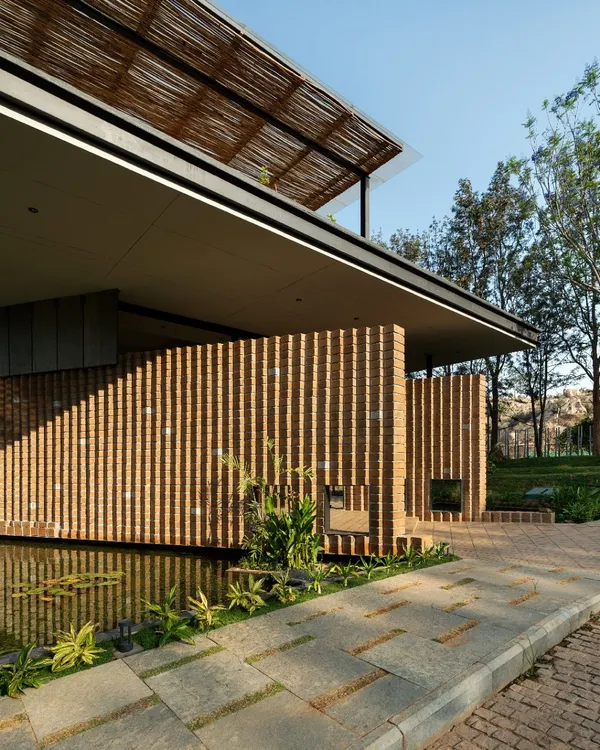 The entrance to 'The Earth' showcases its signature pleated walls made from Compressed Stabilised Earth Blocks (CSEB). The texture and warmth of the brick are balanced by a calm water feature and stone pavers, immediately grounding the building in its natural setting.