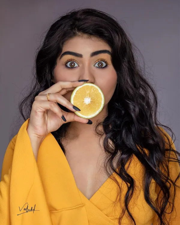 A fun and quirky close-up portrait using a slice of orange. The bright yellow of the fruit, outfit, and eyeshadow creates a vibrant, monochromatic theme that makes the model's expressive eyes the center of attention.