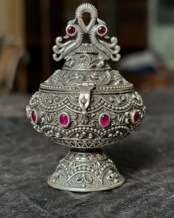 Our antique-finish silver kumkum box, shown closed to highlight the ornate peacock design on the lid. Studded with pink stones, this piece is a beautiful and traditional wedding or housewarming gift.