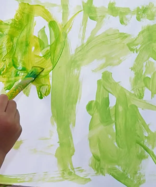 Little hands and busy minds at work. This close-up shows a child exploring shades of green, learning about color mixing and brush strokes in a free and expressive way.