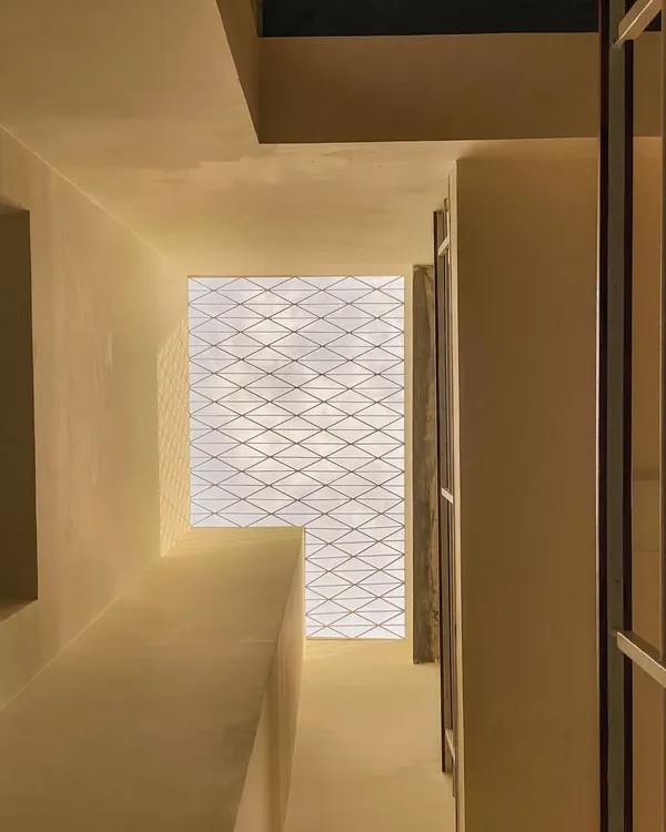 A view looking up through a light well in the Tripathy residence. The simple grill on the skylight creates a delicate, shifting pattern of shadows on the walls below, adding a layer of texture and interest.