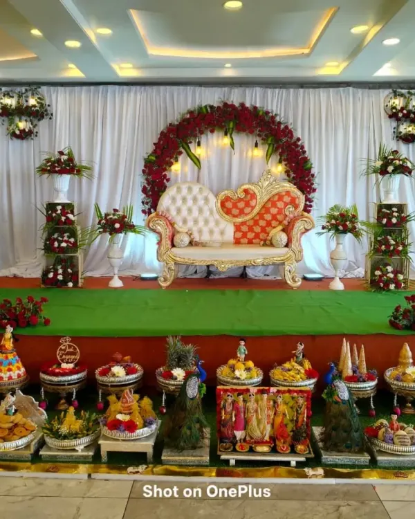 This is a complete stage and Seer Thattu setup I designed for a traditional ceremony. The grand floral arch with deep red roses, elegant white and red diwan seating, and the meticulously arranged offering plates in the front create a rich, festive look.