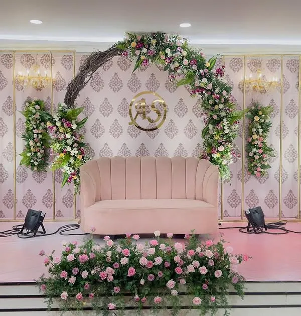 This stage combines rustic and elegant elements for a unique engagement ceremony backdrop. I used a natural twig arch intertwined with lush roses and orchids, set against a classic patterned wallpaper and complemented by a modern pink velvet sofa for the couple.