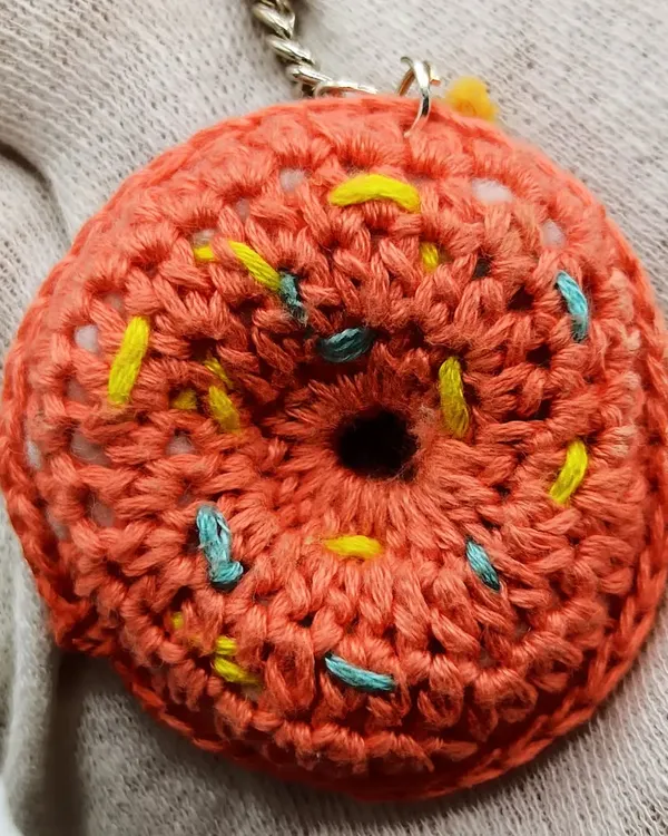 A donut a day keeps the sadness away! This is a close-up of my crochet donut keychain, showing the textured 'glaze' and colorful yarn 'sprinkles'. It's a sweet treat that lasts forever.