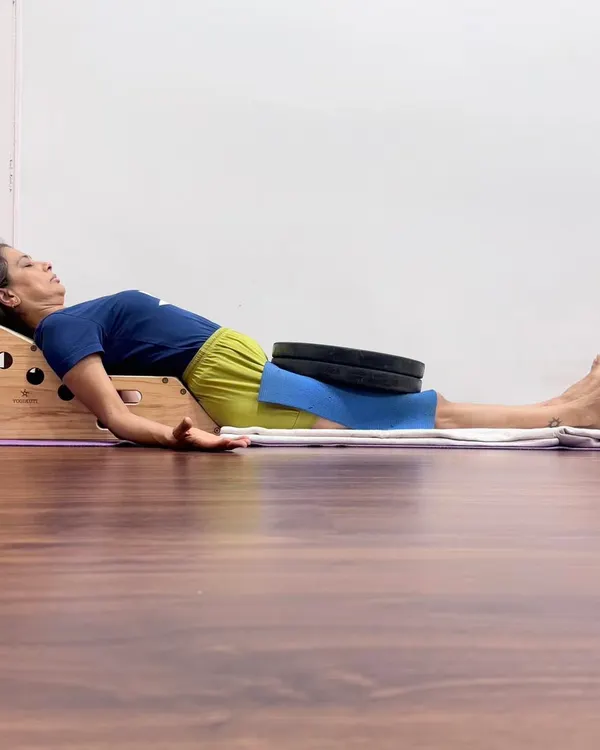 Supported Savasana on a Simhasana Box with weights on the thighs. This setup gently arches the upper back to open the chest, deepens the breath, and grounds the body to calm the nervous system.