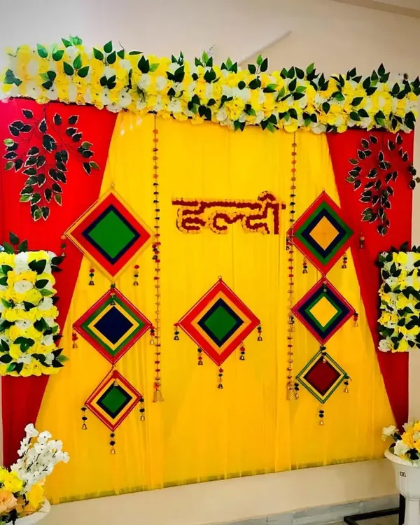 This is a traditional Haldi backdrop I set up at a client's home. It combines bright yellow and red drapes, topped with artificial marigold garlands and decorated with colorful hanging tassels for a truly festive look.