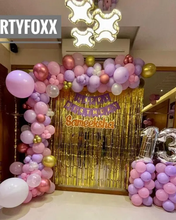 A beautiful at-home 13th birthday decoration for Sameeksha. The setup includes a gold sequin backdrop and a pink and purple balloon arch with silver number balloons.