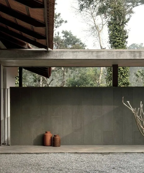 The entrance to the Polibetta Farmhouse, where a minimalist design meets the lush Coorg landscape. A long Kota stone-clad wall guides visitors and frames the entry court, hinting at the views beyond.