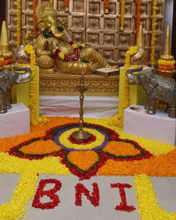 A traditional Ganesha installation for a BNI corporate meet. The decor includes a large floral rangoli on the floor spelling out "BNI," seamlessly integrating the company's identity into the festive design.