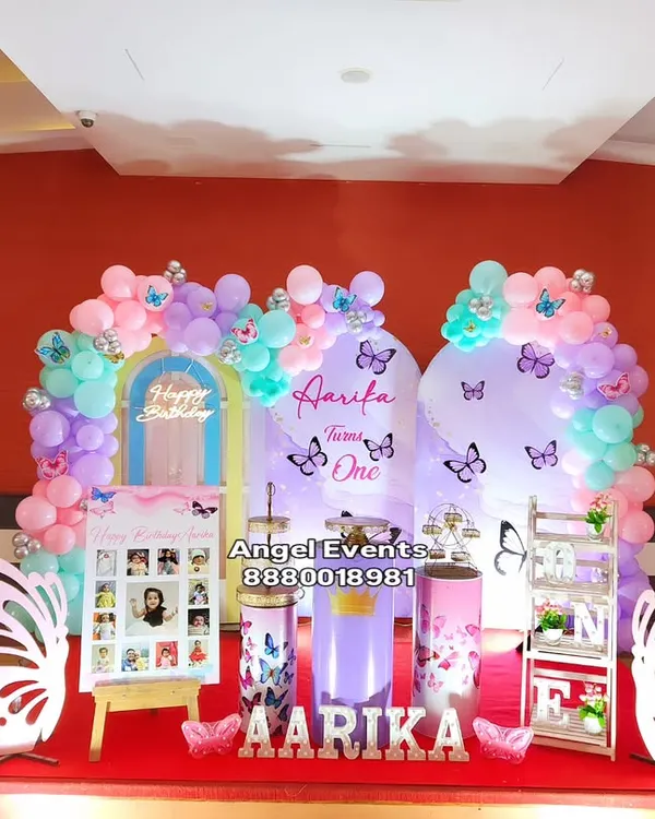 A beautiful butterfly theme for a first birthday, featuring two arched backdrops, a pastel balloon garland, and large white butterfly wing cutouts.