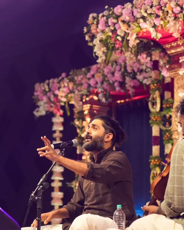 An energetic shot of singer Sid Sriram performing live on stage at the ISKCON Whitefield Janmashtami event, capturing his passion and the beautiful floral stage decor.