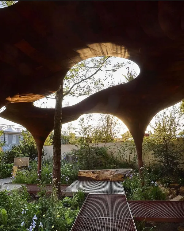 This is an example of a highly artistic, custom-fabricated pergola. The organic, curved cutouts in the wooden canopy allow natural light to filter through while creating a unique sculptural statement in the garden.