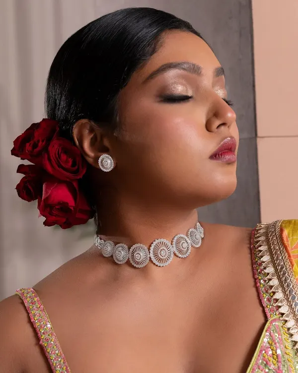 A high-fashion look for a jewellery campaign, inspired by a "desi Frida Kahlo" mood. The makeup is centered around a bold, berry-stained lip and glowing skin, with hair styled into a classic bun adorned with deep red roses for a dramatic and artistic feel.