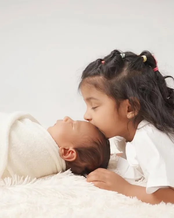 A touching moment of sibling love as a big sister gently kisses her newborn sibling's forehead.