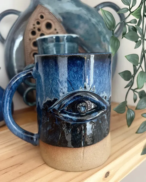 This evil eye mug is a powerful and beautiful piece, designed to bring a sense of protection. The deep blue glaze is layered to create depth around the eye, making it a truly striking handmade ceramic mug.