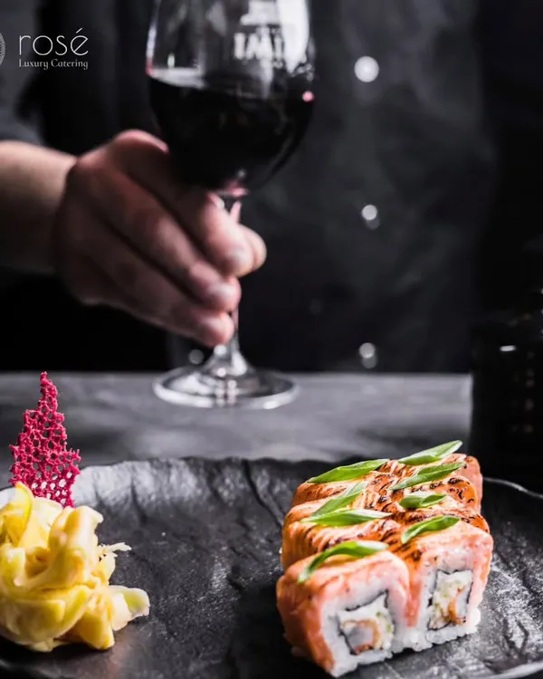 We are ready to elevate your special occasions with our premium catering services. This image of a sommelier with a glass of red wine and a plate of sushi captures the sophisticated dining experience we offer.