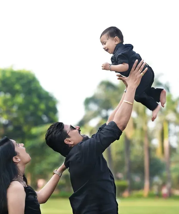 A classic, joyful family moment captured outdoors. A father lifts his child high in the air while the mother looks on, creating a dynamic and love-filled portrait.