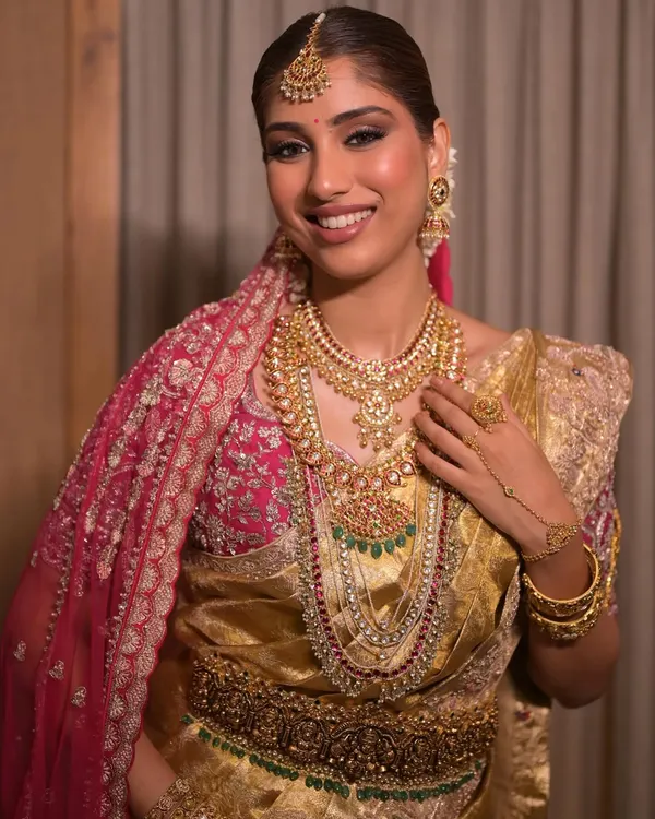 A stunning South Indian bridal look featuring a golden Kanjeevaram saree and layers of traditional temple jewelry. The makeup is soft glam, with defined eyes and radiant skin to complement the richness of her attire.