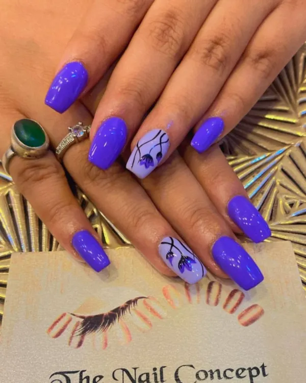 A beautiful set of square nails in a vibrant purple. The ring fingers are accented with a lighter lavender base and delicate, hand-painted purple flowers.