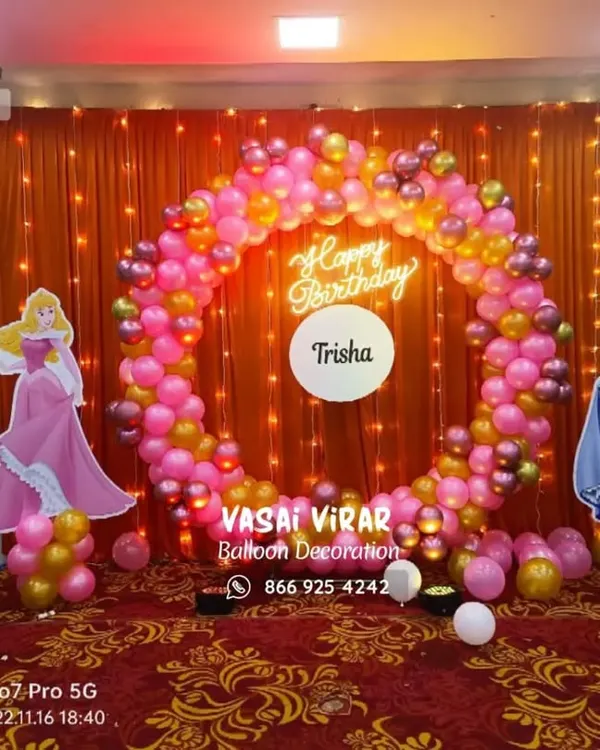 A royal celebration for little Trisha's first birthday. This princess theme features a beautiful balloon ring in pink and gold, life-sized cutouts of Cinderella and Aurora, and a glowing marquee number '1'.