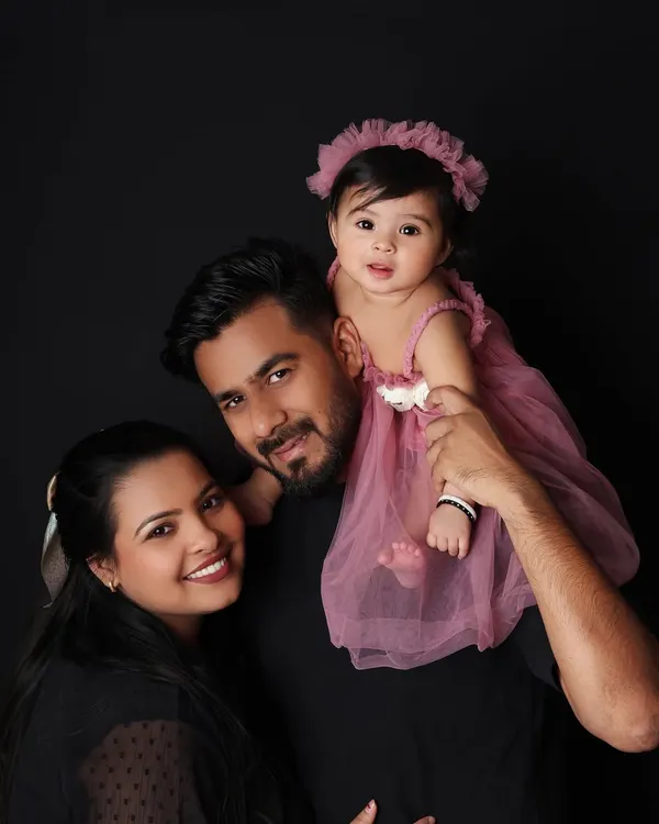 A classic family portrait against a simple black background. The focus is entirely on the family's connection, with the father holding his daughter on his shoulders.