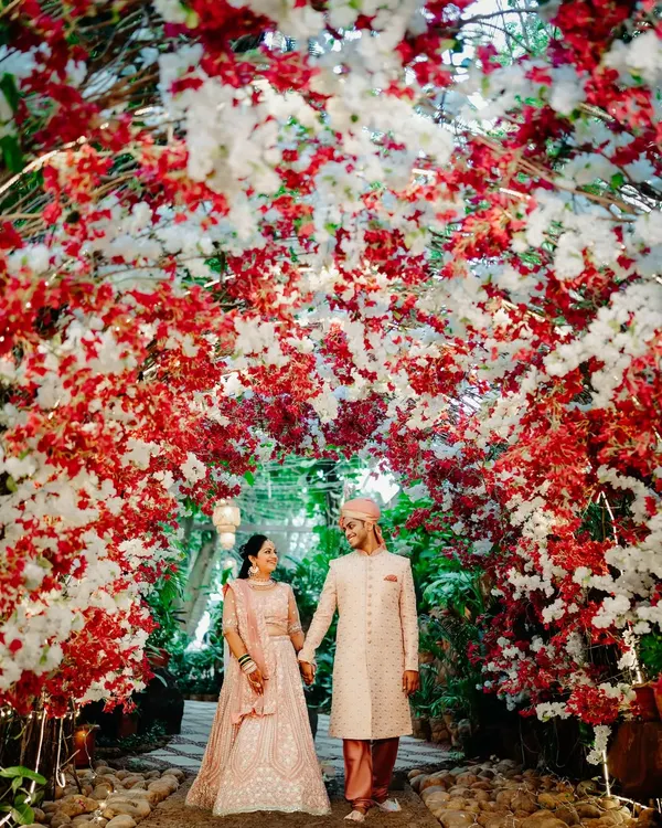 A romantic portrait of the couple framed by a stunning red and white floral arch. The way they look at each other captures the magic of the moment.