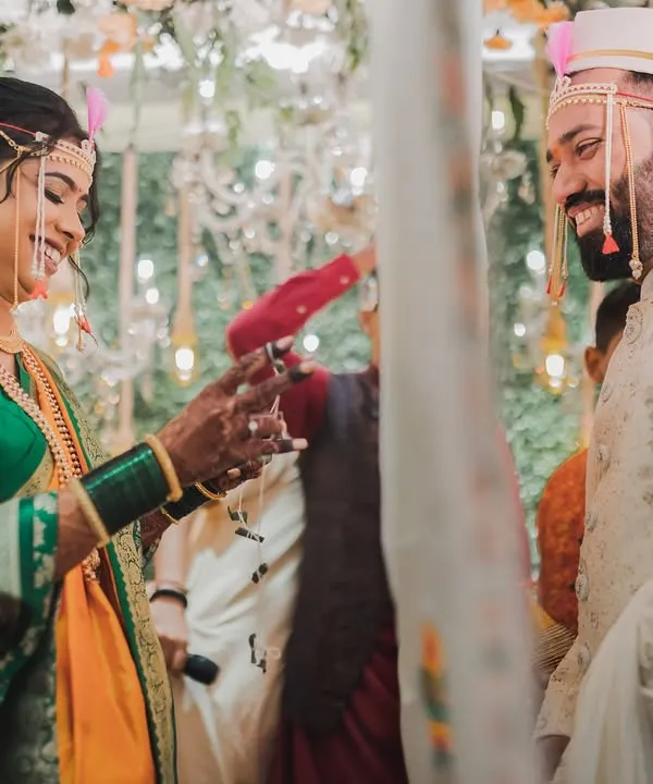A beautiful moment from a traditional Marathi wedding, capturing the playful interaction between the bride in her Nauvari saree and the groom.