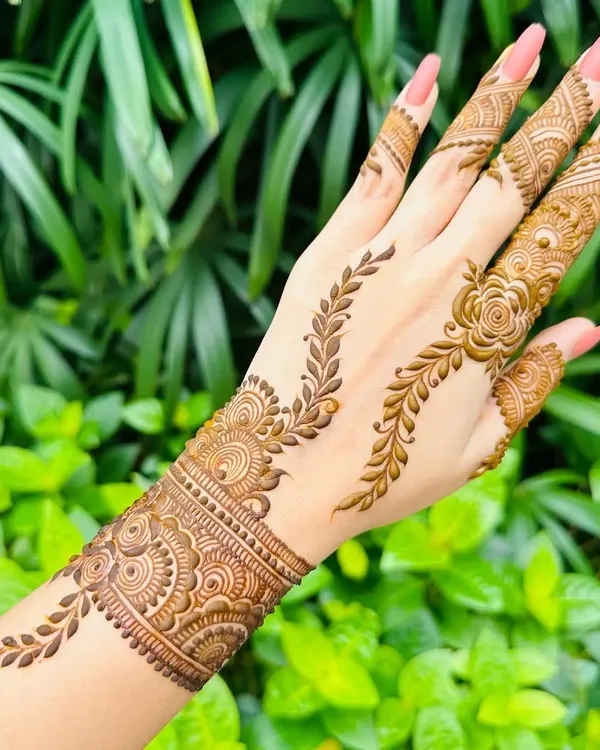 This elegant design features a leafy vine pattern that trails up the finger, connected to a beautiful wrist cuff. It's a perfect example of a modern and chic party mehandi.